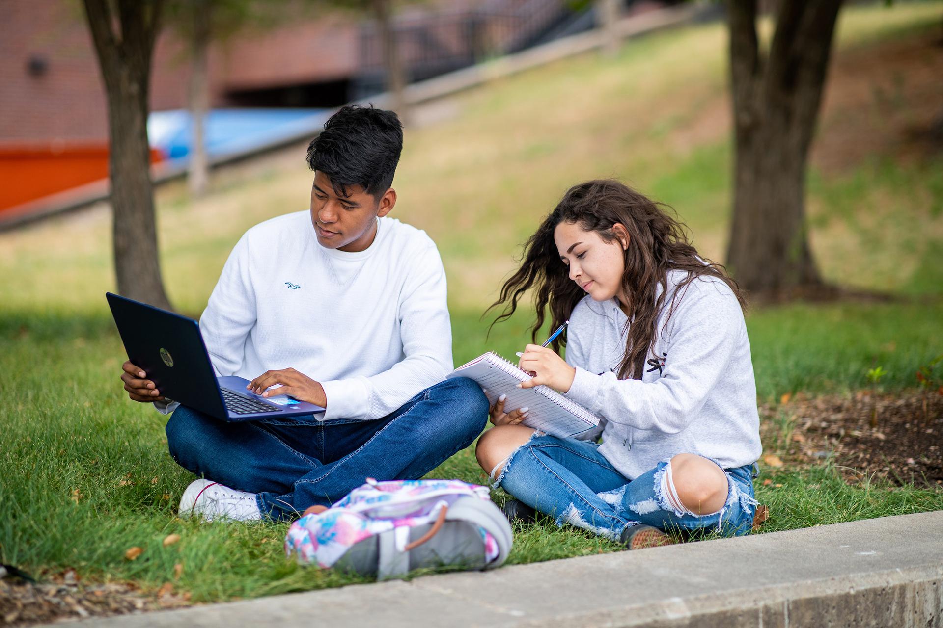 Two young students studying in a grassy area