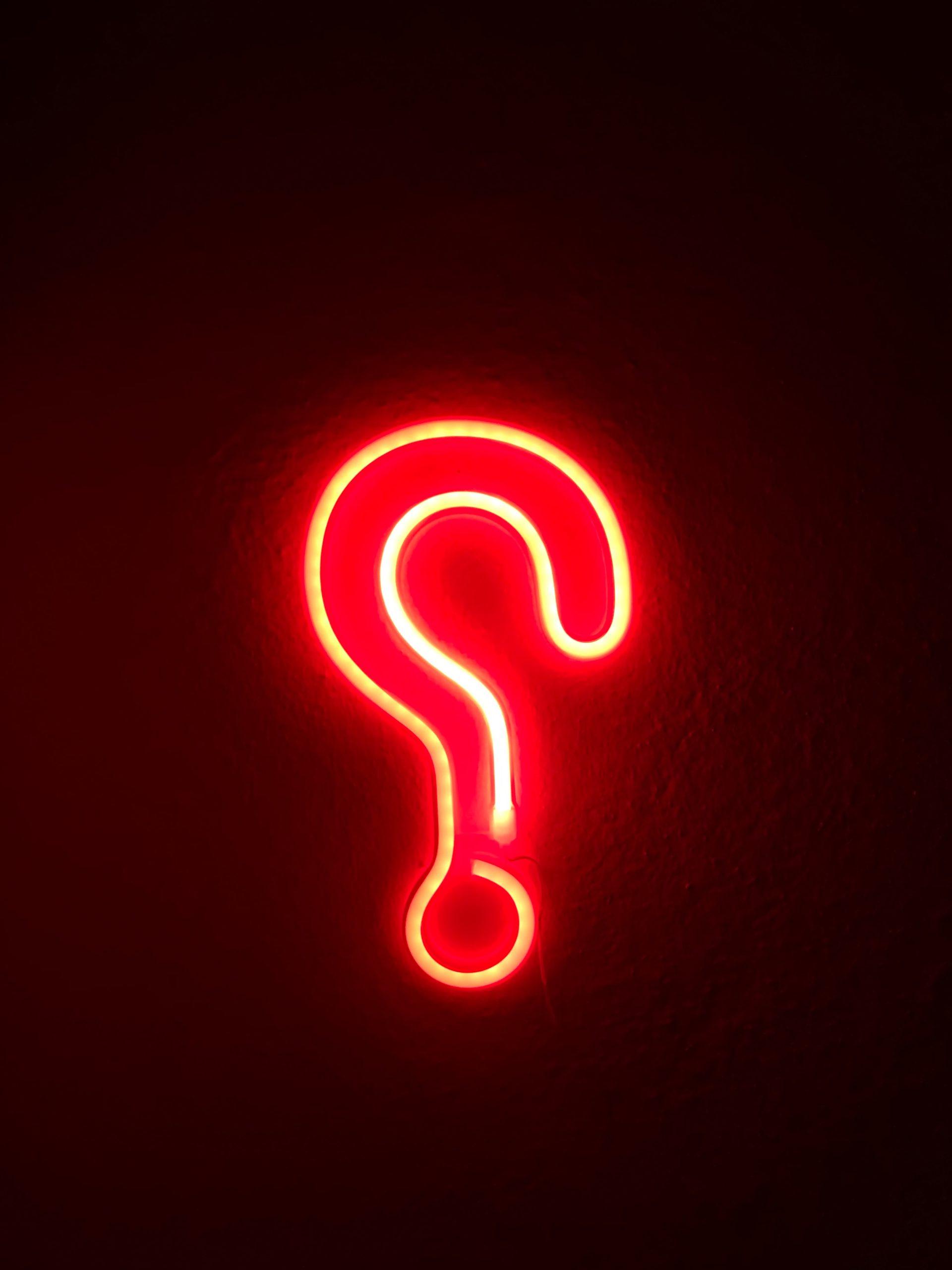 A red neon sign shaped as a question mark against a dark wall