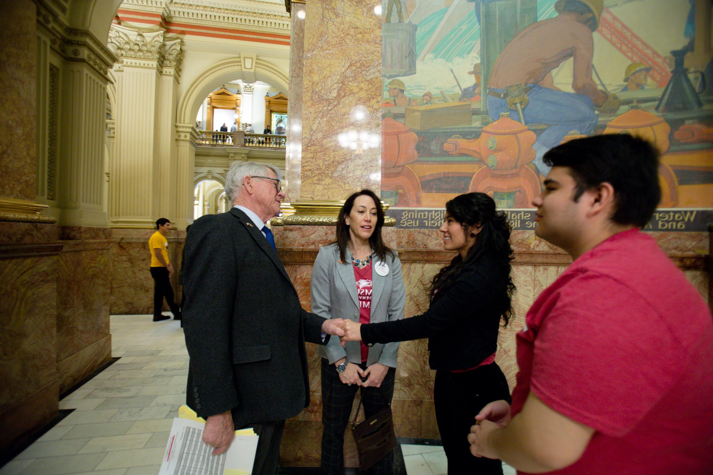 Female student shaking hands with a politician inside the state capitol.