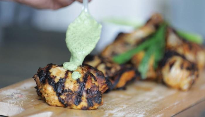 Close-up of cilantro sauce being spread over grilled chicken.